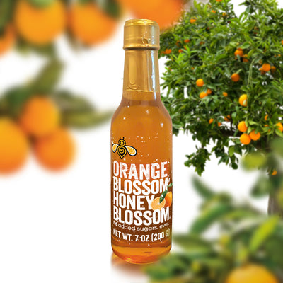 A 7 oz glass bottle, filled with extra light amber honey, surrounded by Orange trees
