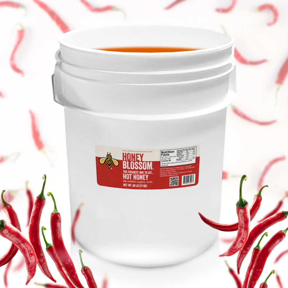 A bucket, filled with hot honey, surrounded by cayenne peppers