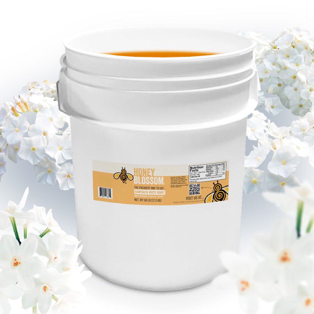 A bucket of extra light amber honey that is surrounded by campanita flowers