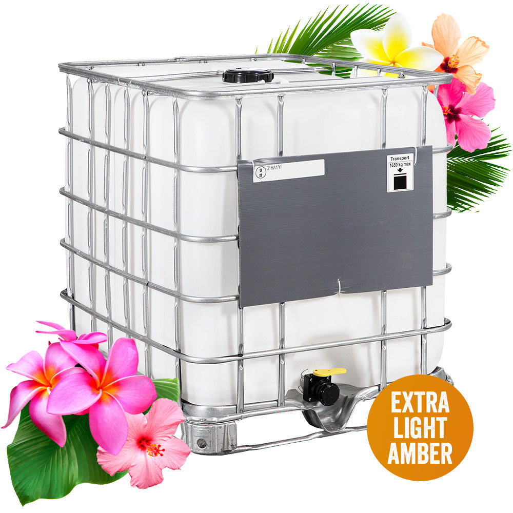 Jungle Honey in a large industrial IBC tote with a protective metal cage, black top cap, and dispensing valve. Surrounded by vibrant tropical flowers, including pink plumeria, hibiscus, and white frangipani, with lush green palm leaves against a clean white background. An orange circular badge identifies the honey's Extra Light Amber color grade.